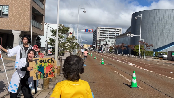 小松駅前で声援した学生たち。手作りのボードでハイタッチを呼びかけた。.PNG